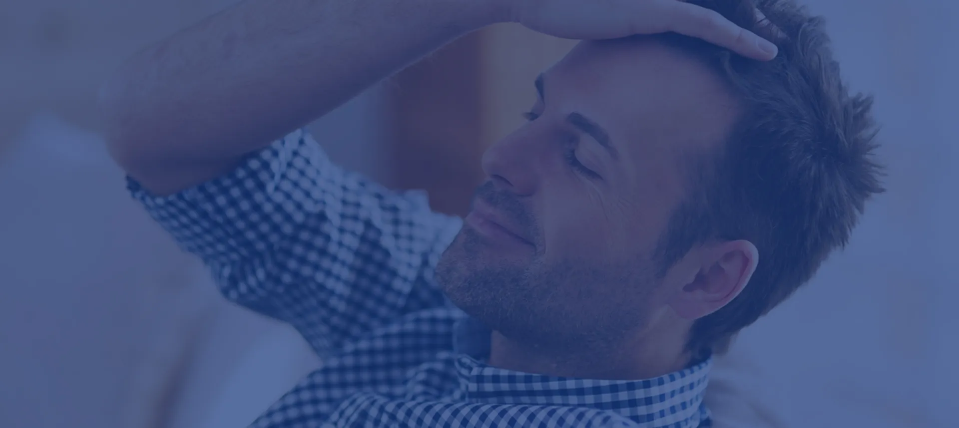 Hombre apoyando la mano en la cabeza con los ojos cerrados, expresión de alivio y satisfacción, cabello corto bien cuidado, camisa a cuadros azul y blanca, ambiente interior claro y acogedor, tono azulado sofisticado superpuesto, iluminación suave, fotografía realista